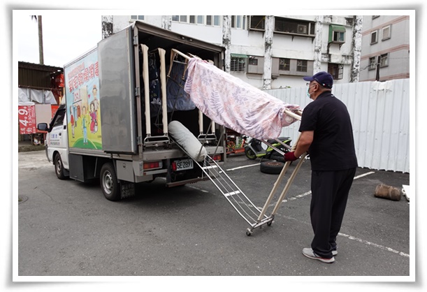 伊甸宜兰干燥消毒车操作人员将案家的被单与衣服上架，进行除湿、消毒与烘干等清洁工作。