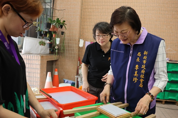 新北市社会局局长李美珍在服务对象的引导下，体验手作手抄纸。